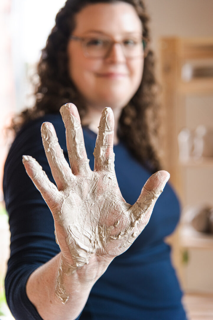 white female potter holding up right hand with dry clay during Halifax Brand Photography shoot with Dandelion Digital