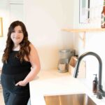 dark haired young woman in black sleeveless jumper, leaning on counter