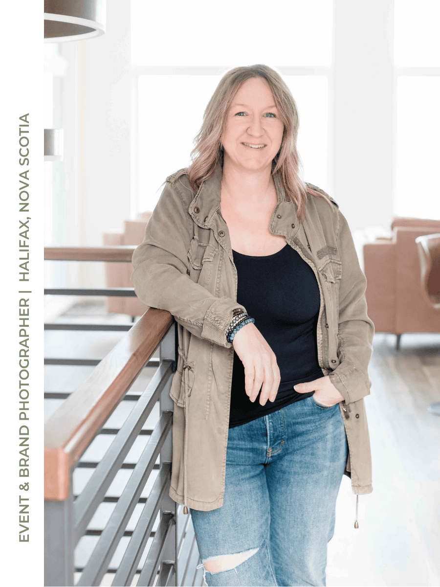 Allison shown leaning against a railing, wearing a black top, olive green jacket and jeans