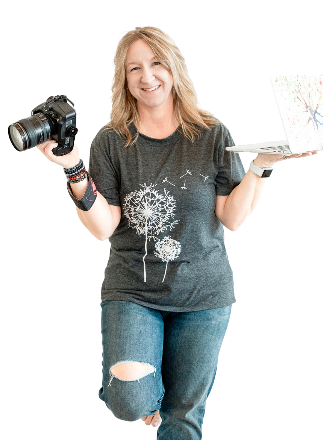 blond photographer in a black tshirt with a white dandelion holding a camera in one hand and balancing a laptop in the other.