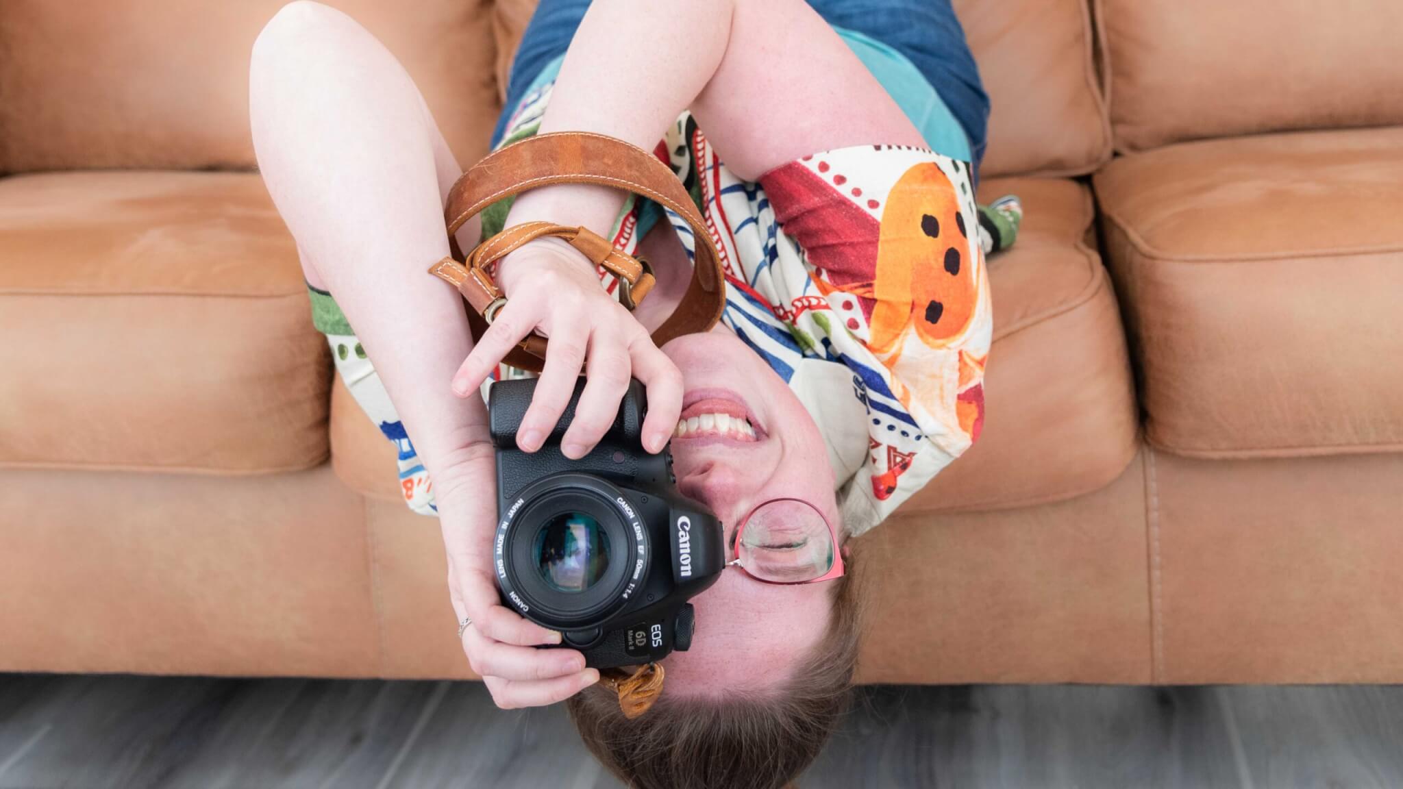 female photographer hanging upside dodwn of sofa while looking through DSLR camera