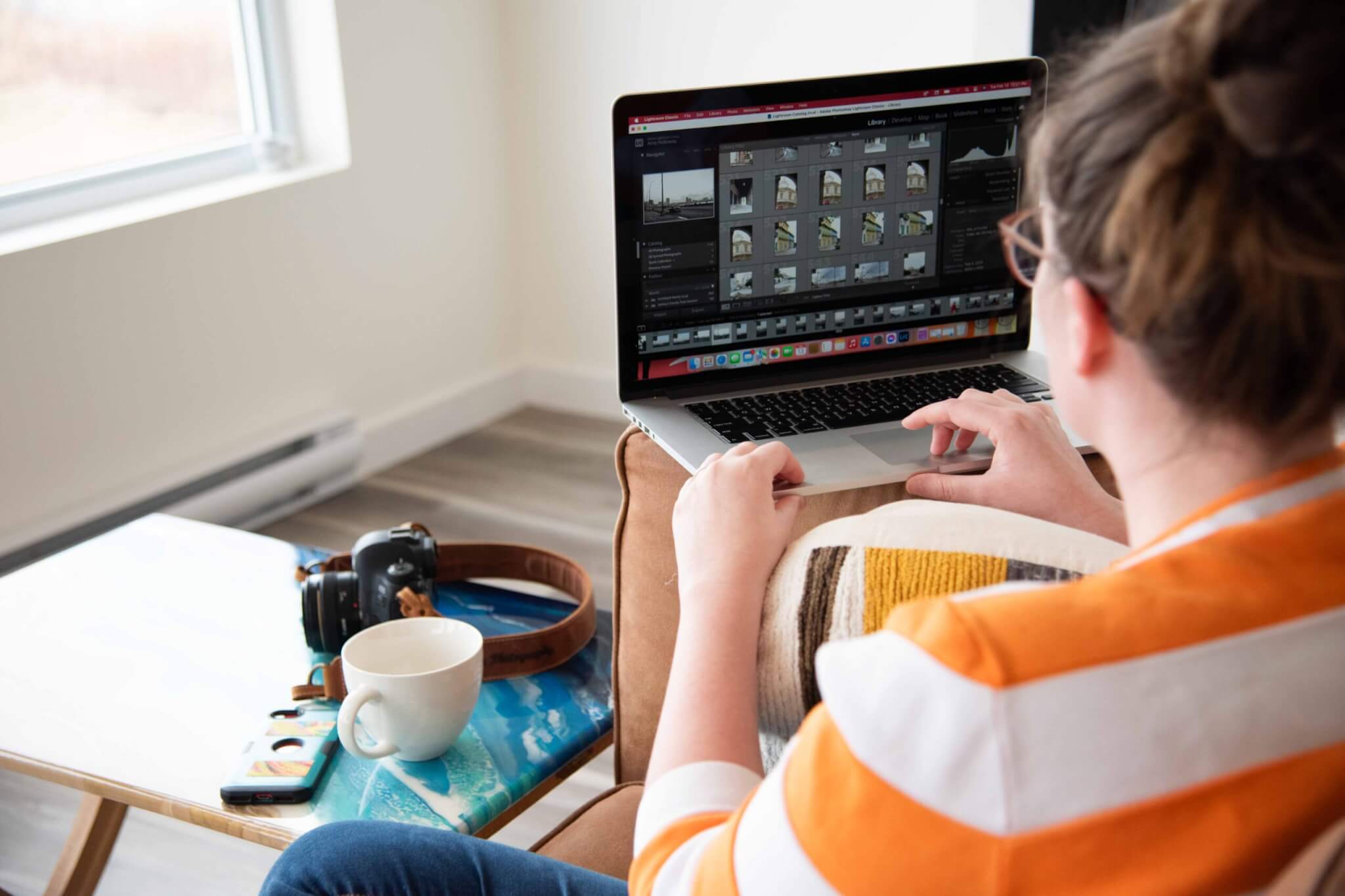 over the shoulder of a female photographer using Lightroom on macbook