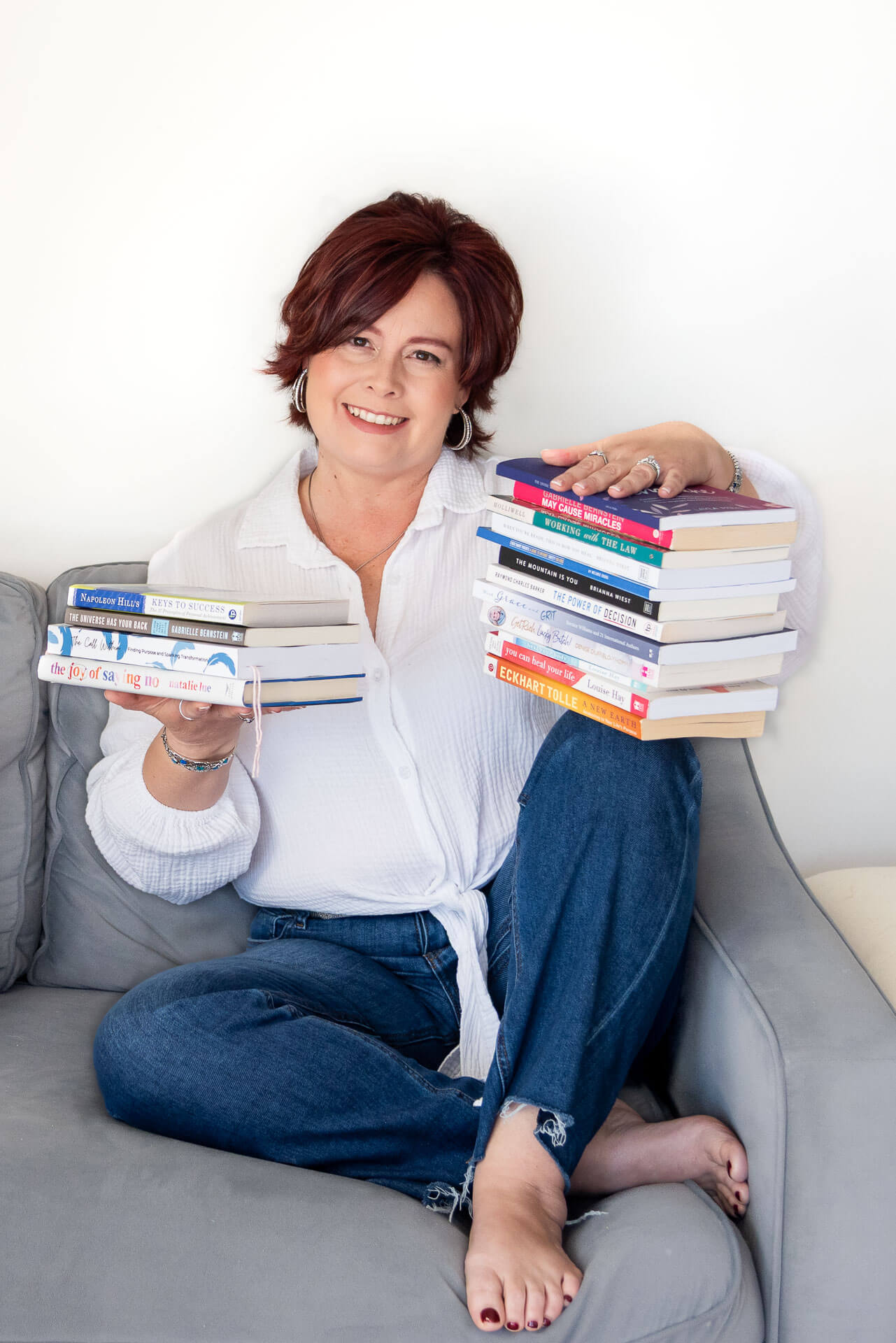 uthor and coach holds two stacks of personal development books that shaped her resilience coaching practice.