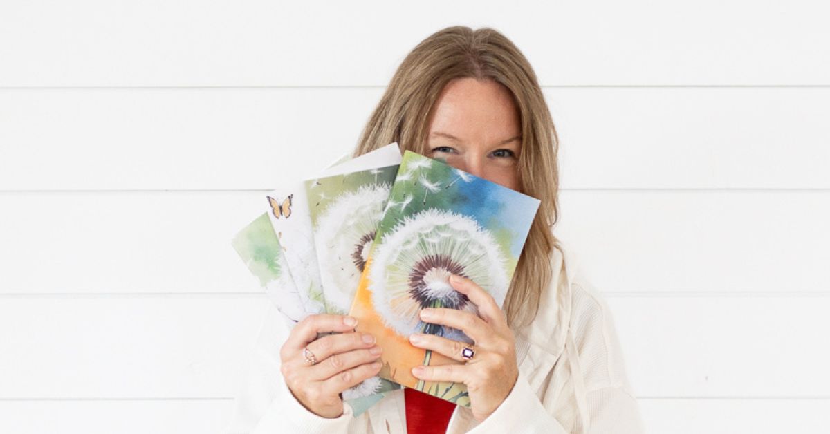 blond woman holding 4 fanned out dandelion journals in front of her face