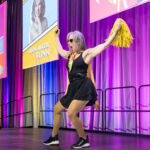 a women on stage in a short black dress with yellow pompoms in her raised arms during movement break at Wonder Women conference, Halifax Convention Centre