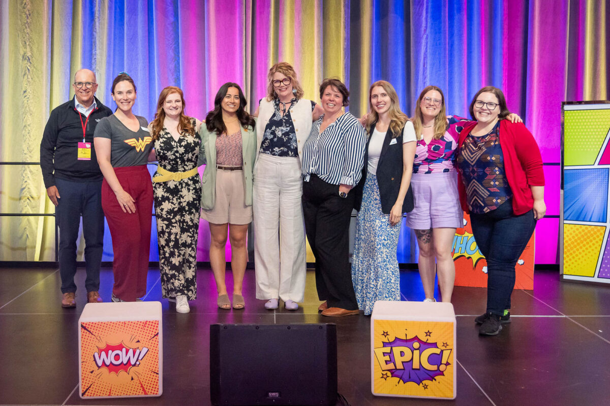 the Halifax Chamber of Commerce planning committee for the Wonder Women conference includes 8 women and a man on a stage with colourful drapes