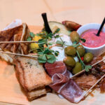 charcuterie board with toast, olives, pink dip, sliced meast