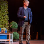 aucasian man in blue blazer on stage speaking at lighthouse Arts Centre, Halifax