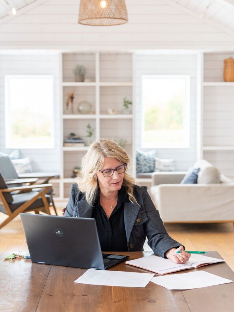 blond woman in dark glasses working at a wood table with a feature wall behind