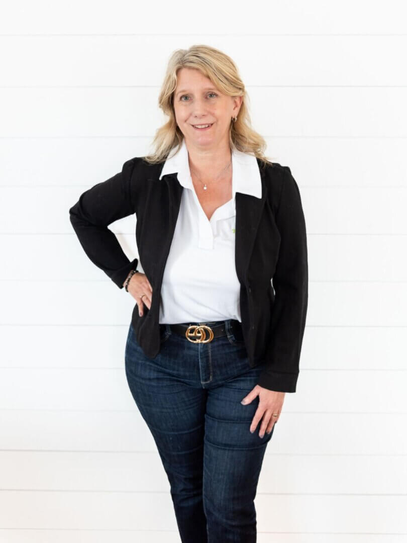 Blond woman in a black suit – 3/4 body pose along a white wall