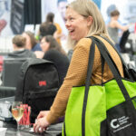 woman reacting hppily at trade show booth, carrying swag bag