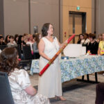 a women in the centre of a crowded room, wearing a white linen dressing, holding a rain stick during Halifax Chamber of Commerce Wonder Women Conference meditation session