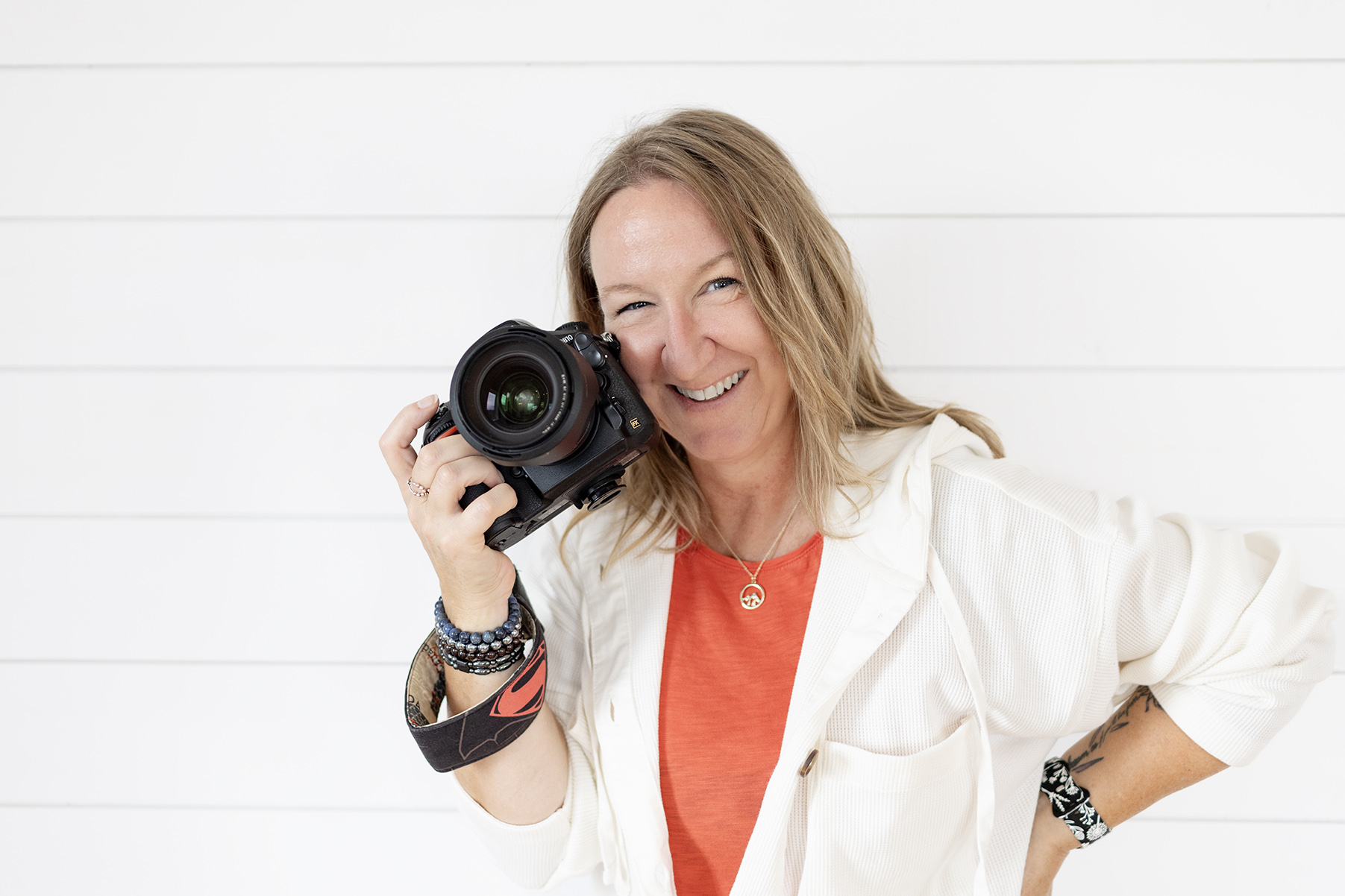 female photographer wearing white and orange holding camera to cheek