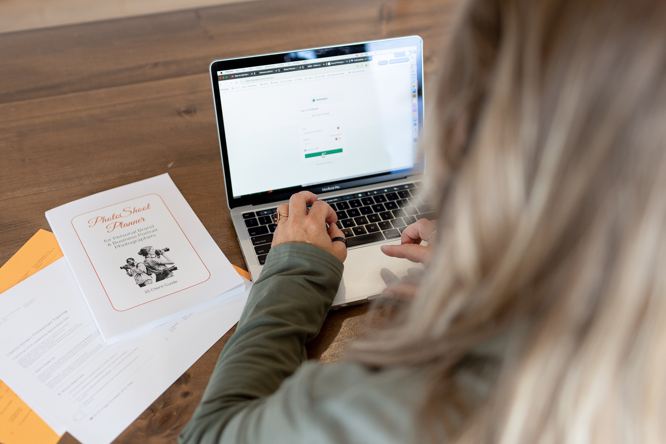 working on laptop in Dubsado CRM with Photoshoot planner on table alongside