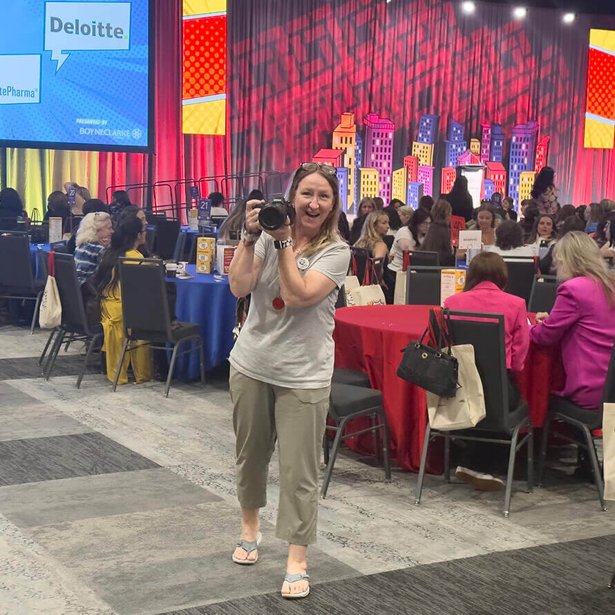 Allison, a blong photographer and founder of Dandelion Digital, holding up her camera in front of a full conference room